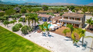 A large house with a swimming pool, surrounded by palm trees and a well-maintained lawn.