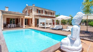 A swimming pool with lounge chairs and umbrellas, a stone building with a balcony, and a white statue.