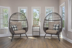 Relax in this serene space with two plush chairs and a small table, surrounded by large windows and a lush plant.