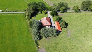 An aerial view of a rural property with a red-roofed house surrounded by green fields and trees.