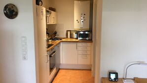 A compact kitchen with a microwave, toaster, and oven. There is a small table with a chair and a power outlet on the wall. - Breekate vacation apartment Gustav - surrounded by greenery (Butjadingen-Tossens)