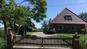 A house with a tiled roof, a car parked in front, and a wooden fence. - Breekate vacation apartment Gustav - surrounded by greenery (Butjadingen-Tossens)