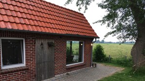 A brick building with a red-tiled roof, a wooden door, and large windows. - Breekate vacation apartment Gustav - surrounded by greenery (Butjadingen-Tossens)