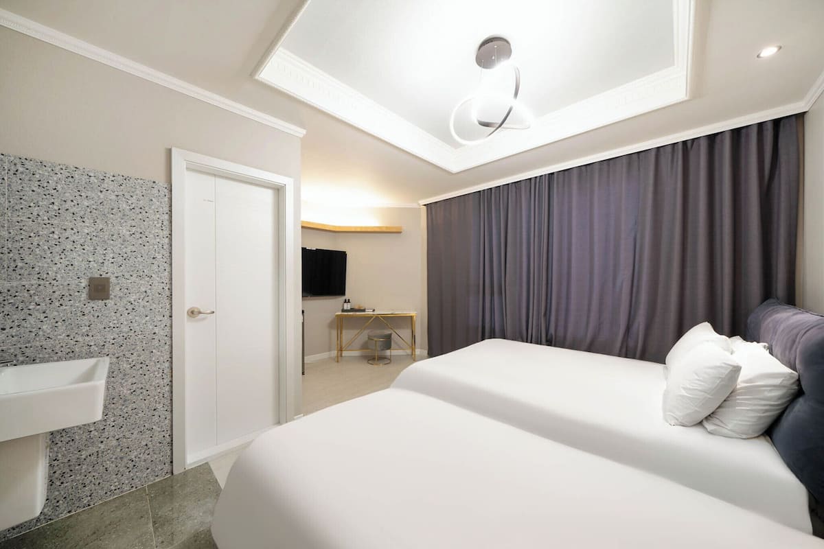A hotel room with a bed, a desk, a chair, a sink, and a ceiling light.