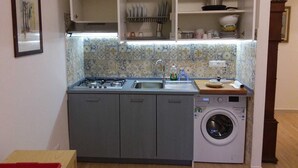 Une cuisine compacte équipée d’une cuisinière à gaz, d’un évier et d’un lave-linge encastré.