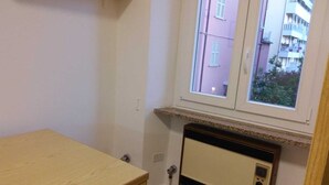 Une pièce avec une table en bois, un radiateur et une fenêtre donnant sur un immeuble rose.