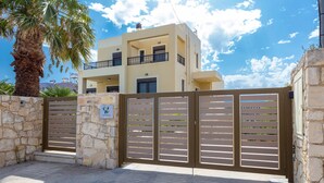 A modern two-story building with a gated entrance, stone walls, and a palm tree. - Villa Selena - Lux 4BD Residence (Chania)