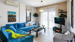 A modern living room with a blue sofa, a coffee table, a TV, and a fireplace. - Villa Selena - Lux 4BD Residence (Chania)