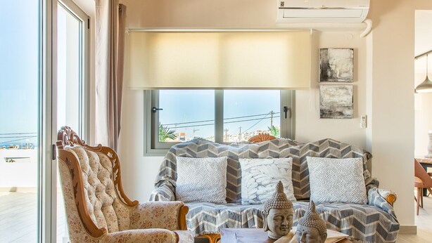 A spacious living room with a wooden ceiling, a large window with a view, a sofa set, a decorative chair, and a small table. - Kismet Apt - Retreat to a Stylish home (Chania)