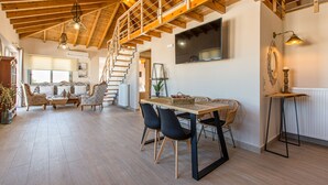 A spacious living area with a wooden ceiling, a dining table with chairs, and a staircase leading to an upper level. - Kismet Apt - Retreat to a Stylish home (Chania)