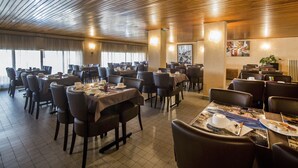 A spacious restaurant with multiple tables and chairs, wooden ceiling, and large windows allowing natural light. - Sampiero Corso (Corte)
