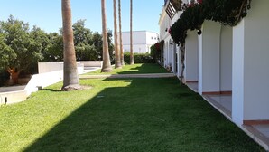 A well-maintained courtyard with a neatly trimmed lawn, palm trees, and a building with white walls and a balcony. - 211- Amazing garden level Apartment - fantastic location (Albufeira)