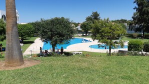 A swimming pool surrounded by greenery, with a clear sky and a building in the background. - 211- Amazing garden level Apartment - fantastic location (Albufeira)