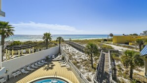 A pool area with lounge chairs, a wooden deck, and a view of the beach and ocean.