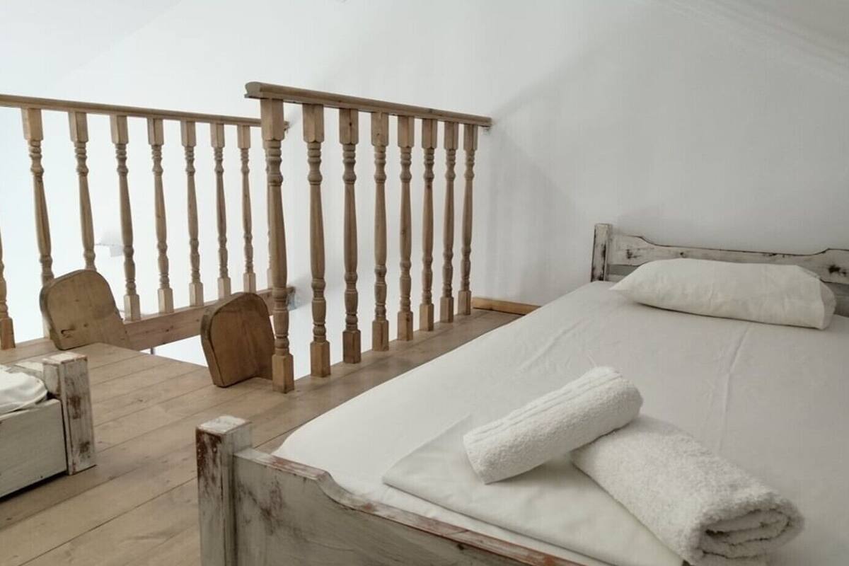 Ein Schlafzimmer mit einem hölzernen Bett, weißer Bettwäsche, einem Holzstuhl und einem Holzbalken.
