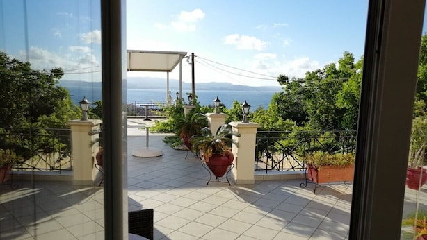 A balcony with tiled flooring, potted plants, outdoor furniture, and a view of the sea and mountains. - Eugenia Studios (Kefalonia)