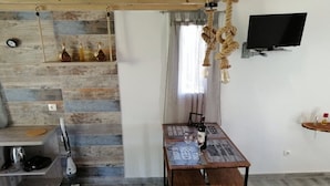 A modern kitchen with a wooden backsplash, a dining table with a placemat, and a TV mounted on the wall. - Eugenia Studios (Kefalonia)