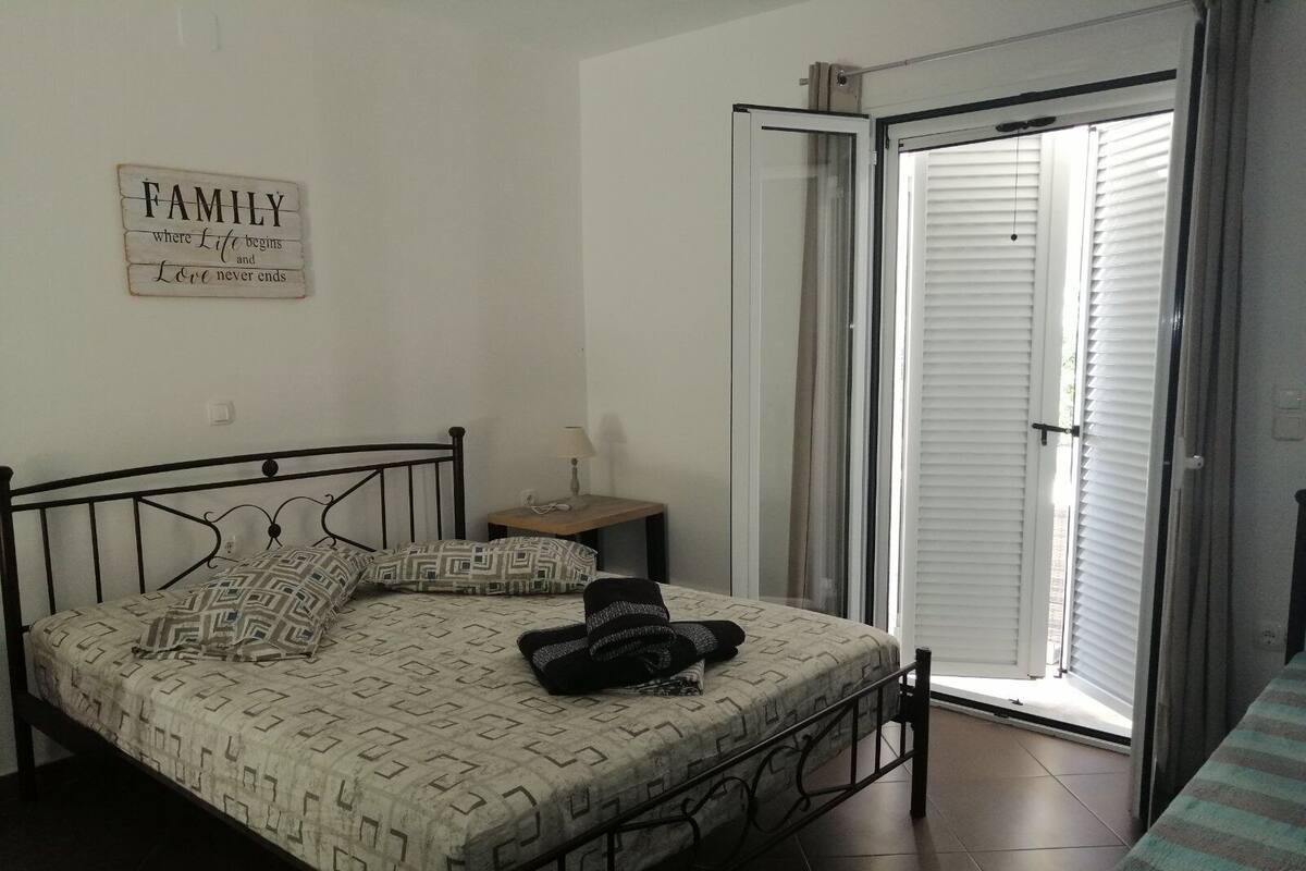 Ein Schlafzimmer mit einem Bett, einem Nachttisch, einer Lampe, einem Fenster mit Jalousien und einem Schild an der Wand.