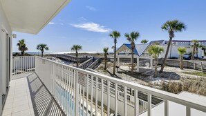 Ein Balkon mit Blick auf einen Strand, Palmen und ein Gebäude mit blauem Dach.