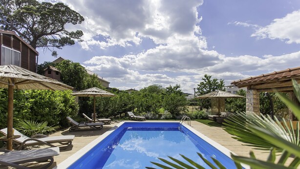 Ein rechteckiger Pool mit Liegestühlen und Sonnenschirmen, umgeben von Grünflächen und Gebäuden.