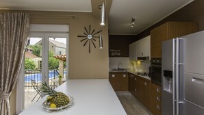 Eine moderne Küche mit einer großen Kochinsel, Edelstahlgeräten und Blick auf einen Balkon mit Sitzmöbeln.