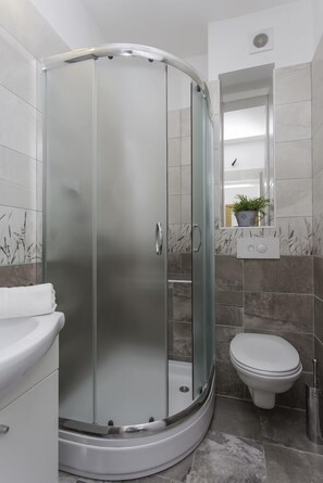 A modern bathroom with a glass-enclosed shower, a toilet, and a vanity with a mirror and a potted plant. - Villa Barbarossa (Kastela)