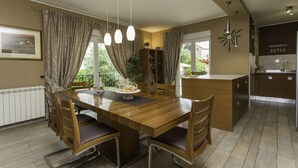 Ein Essbereich mit Holztisch und Stühlen, einem Buffet mit Glaskuppel und Blick ins Freie durch große Fenster.