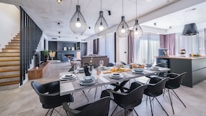 A modern kitchen with a dining area, featuring a long table set for six, black chairs, and pendant lights. - Villa Antonia (Kastela)
