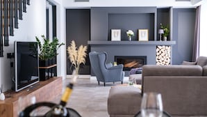 A modern living room with a fireplace, grey sofas, a television, and a wine bottle on the table. - Villa Antonia (Kastela)