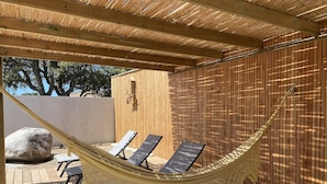 A hammock suspended over a wooden deck with two lounge chairs, a large rock, and a wooden wall. - NEW HOUSE VILLA PORTO VECCHIO (Porto-Vecchio)