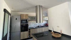 A modern kitchen with stainless steel appliances, a wooden island, and a black countertop. - NEW HOUSE VILLA PORTO VECCHIO (Porto-Vecchio)