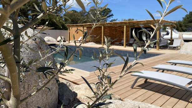 A poolside area with lounge chairs, a wooden deck, and a building in the background. - NEW HOUSE VILLA PORTO VECCHIO (Porto-Vecchio)