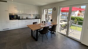 A modern kitchen with white cabinets, a wooden dining table, and a large sliding glass door leading to a patio.