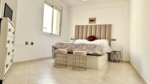 A bedroom with a bed, two stools, a desk, a TV, and a window. - such as beach (Roquetas de Mar)