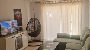 A living room with a television, a round hanging chair, a sofa, and a coffee table. - such as beach (Roquetas de Mar)