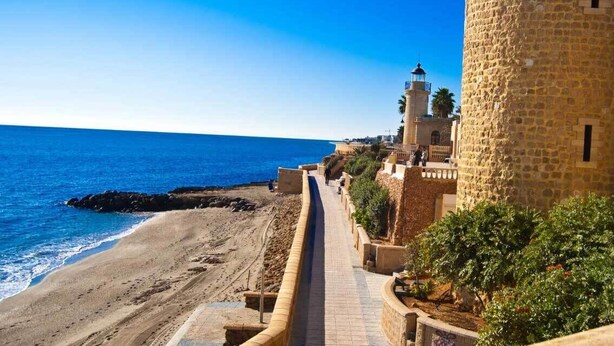 A coastal pathway leading to a lighthouse and a stone tower, with a beach and ocean in the background. - such as beach (Roquetas de Mar)