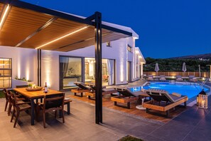 A modern outdoor pool area with lounge chairs and a dining table. - TreeTop Villa I, Private Pool, BBQ & Playground, close to Beach & Shops (Loutra, Rethymno)