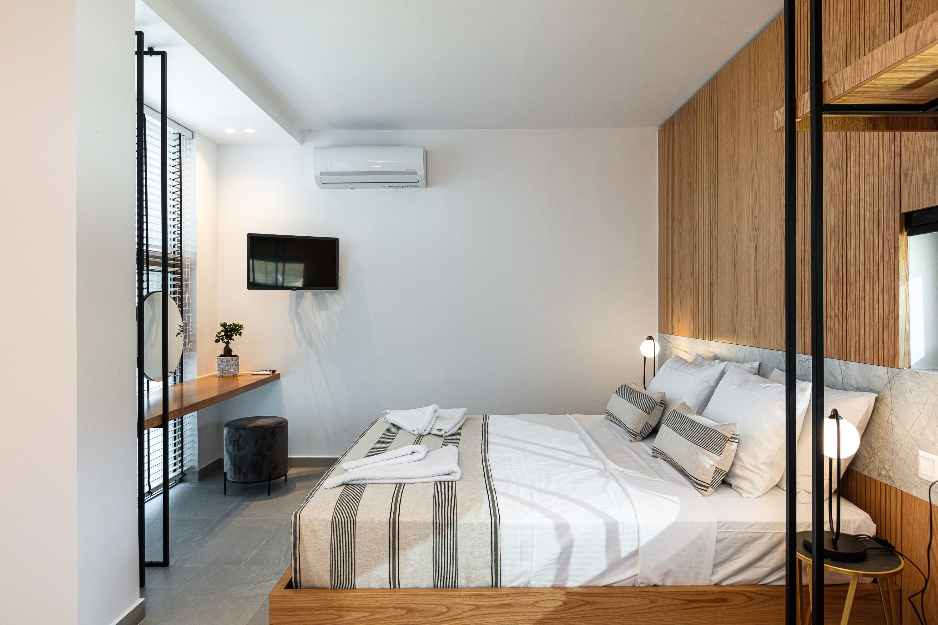 A modern bedroom with a bed, bedside tables, a TV, and an air conditioning unit.