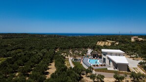 Eine moderne Villa mit Swimmingpool, umgeben von üppiger Vegetation und freiem Blick auf das Meer.