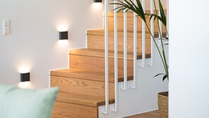 Eine Treppe mit Holzsitzstufen und weißen Geländern, beleuchtet von Wandleuchten.