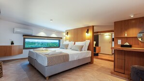 Ein modernes Schlafzimmer mit einem großen Bett, Blick ins Freie, einem Holz-Waschtisch und einer kleinen Sitzecke.