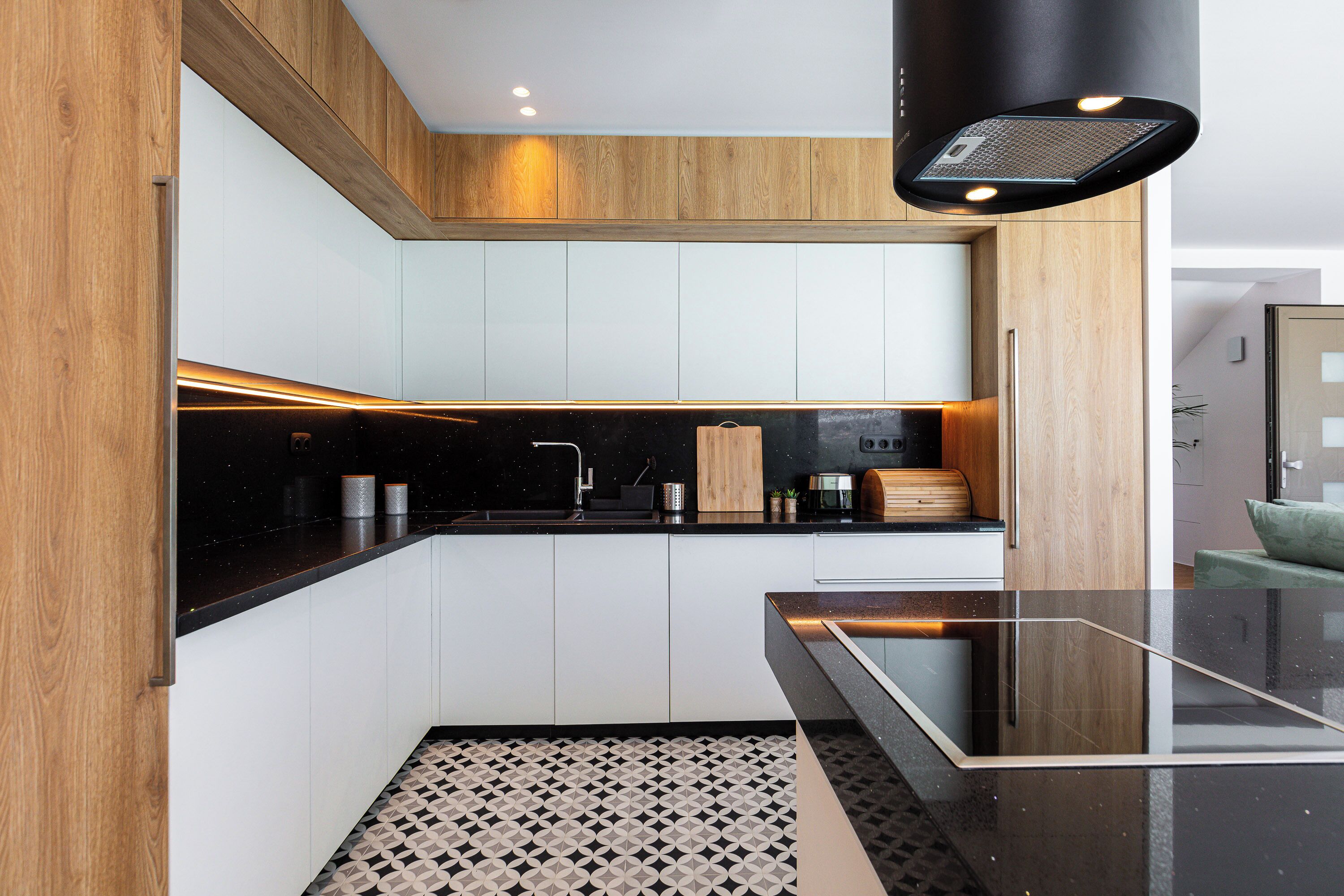 A modern kitchen with wooden cabinets, a black countertop, and a patterned floor.