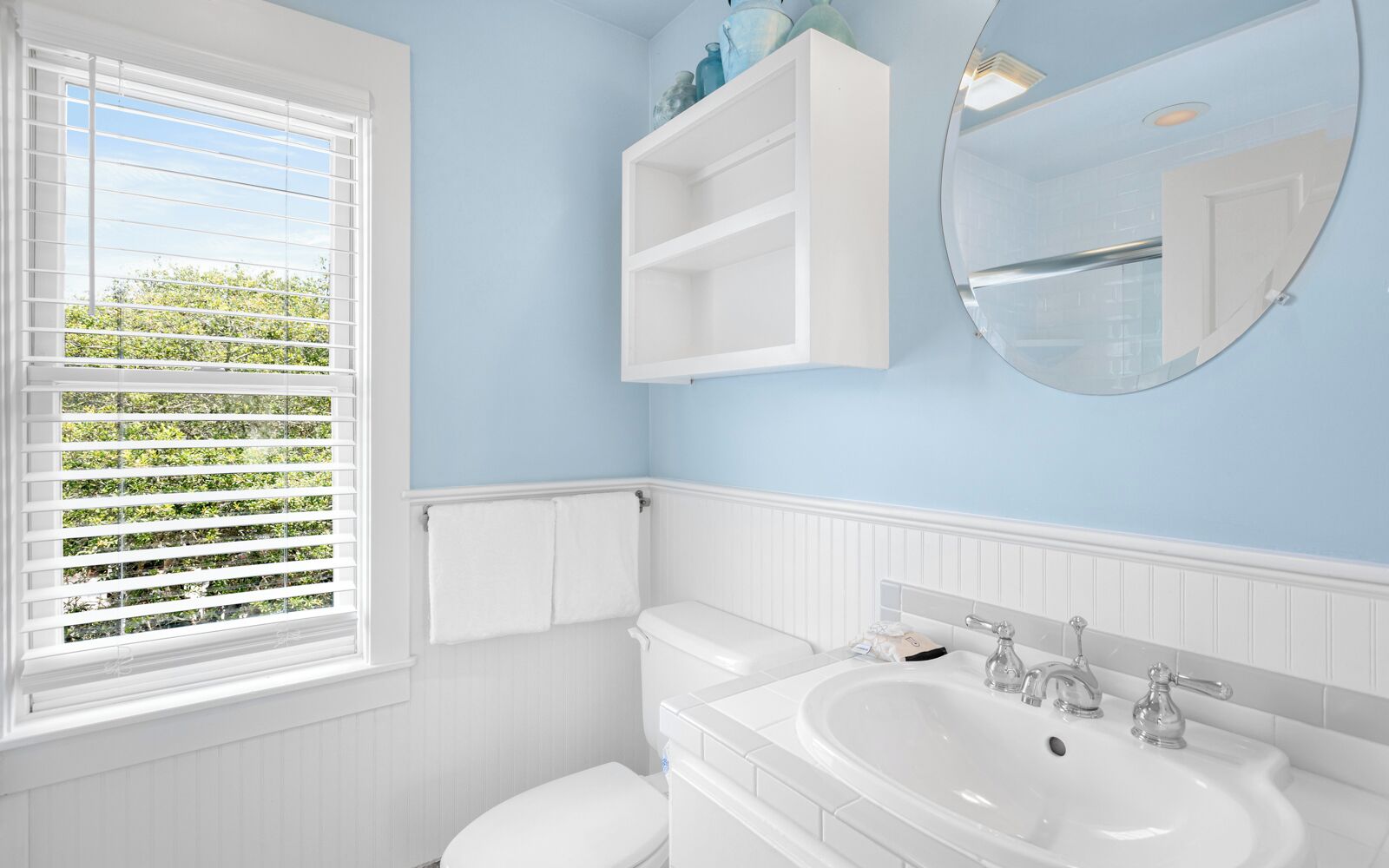 A bathroom with a toilet, sink, and window with blinds.