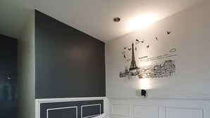 Un dormitorio con cama, cabecera, pared con mural de paisaje urbano y una lámpara en el techo.