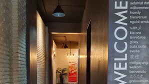 Un pasillo con un cartel de 'WELCOME' en varios idiomas, una pared de ladrillo y una lámpara colgante.