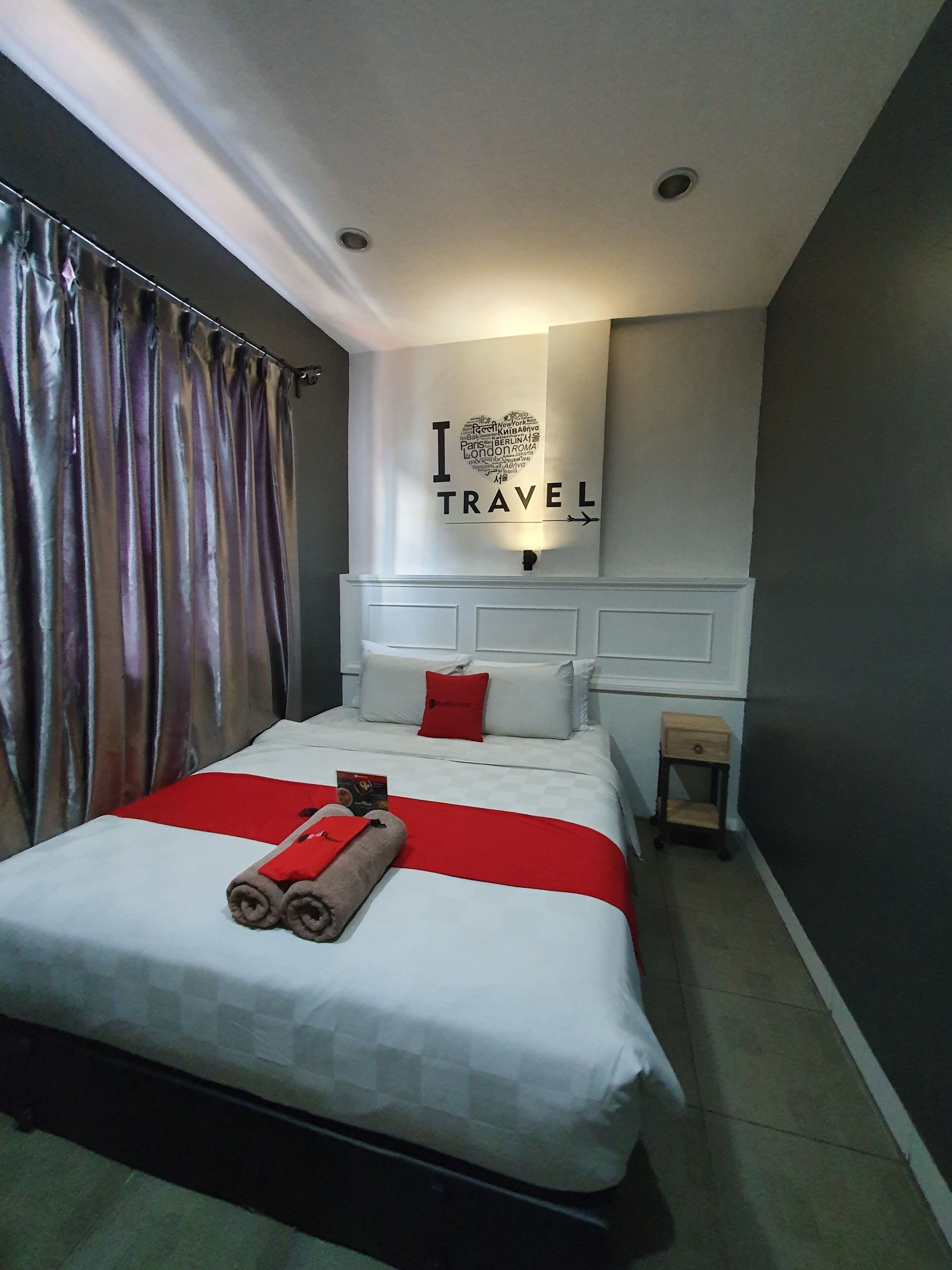 Una habitación de hotel moderna con una cama grande, una colcha blanca y roja, un almohadón rojo y un letrero en la pared que dice 