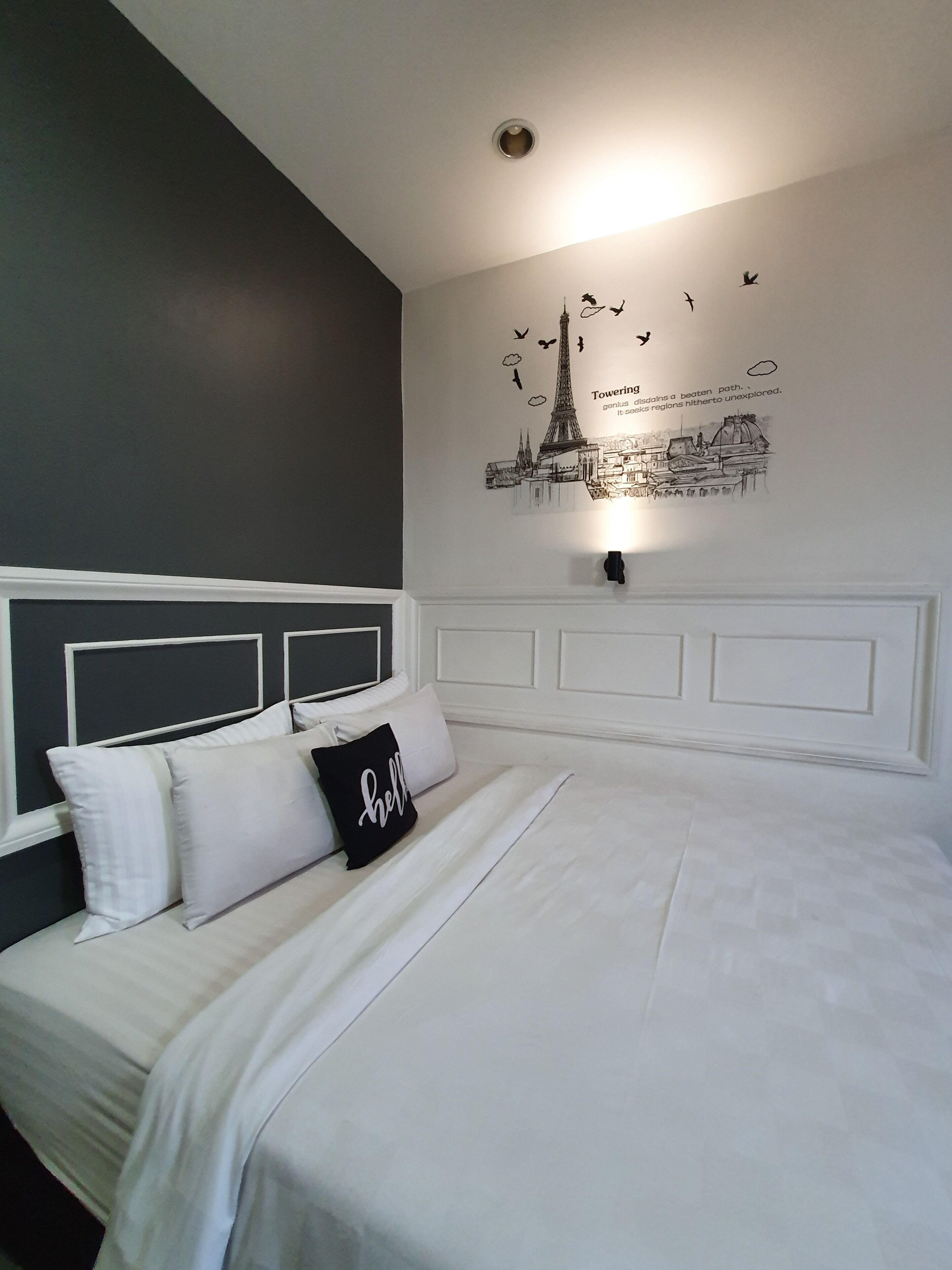 A neatly made bed with white bedding and a black pillow with the word "hello".