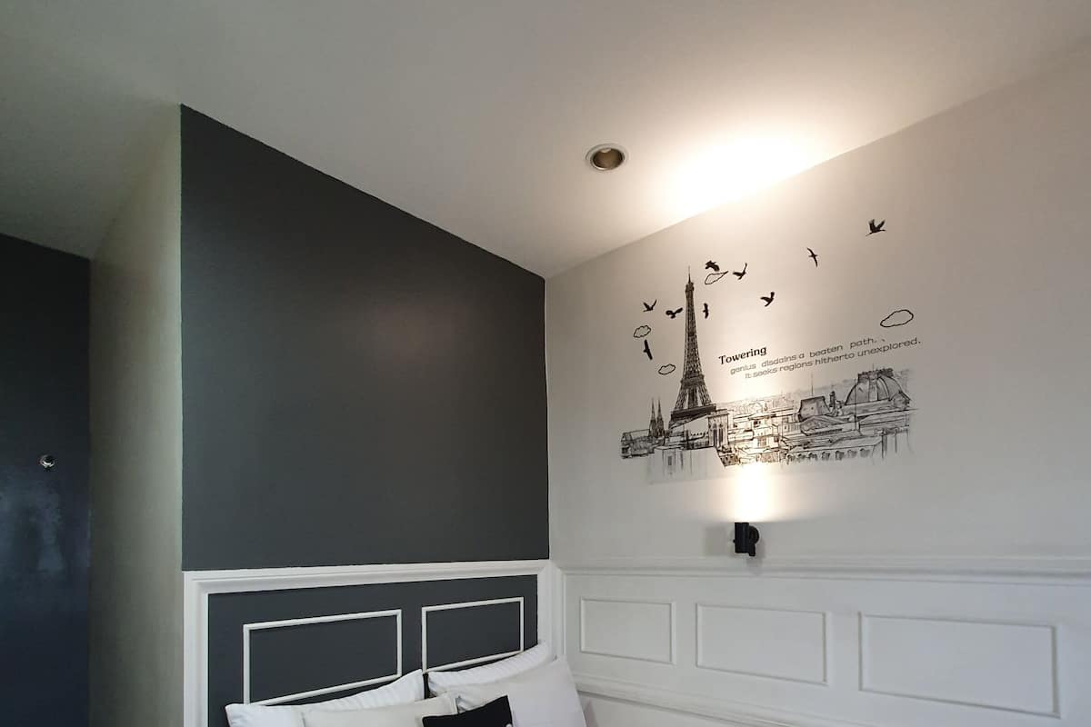 A bedroom with a bed, a headboard, a wall-mounted light, and a cityscape mural.