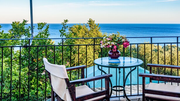 A balcony with a table and chairs, overlooking a body of water and greenery. -  Eros Cozy, Panoramic Sea View, Perfect Location (Pylos-Nestoras)