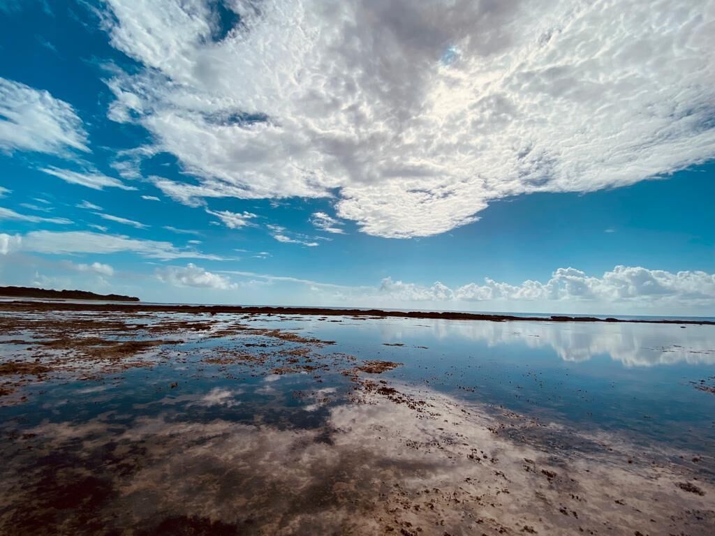 A wide, reflective water surface with a clear sky and scattered clouds.